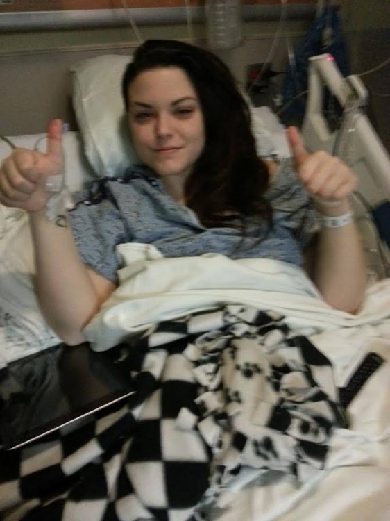 Christina in a hospital bed, giving the thumbs up