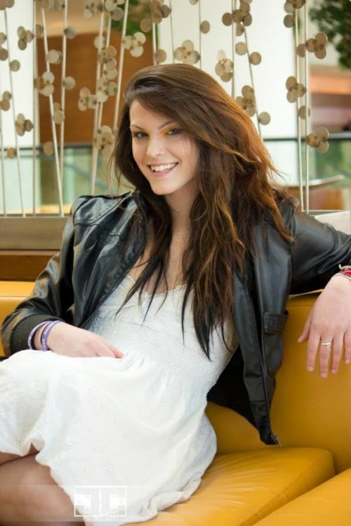 Christina in a white dress and black jacket, sitting on a yellow couch