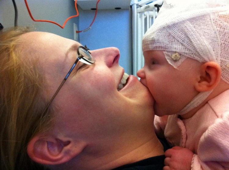 A baby with a bandage on his head kisses his mom's chin. 