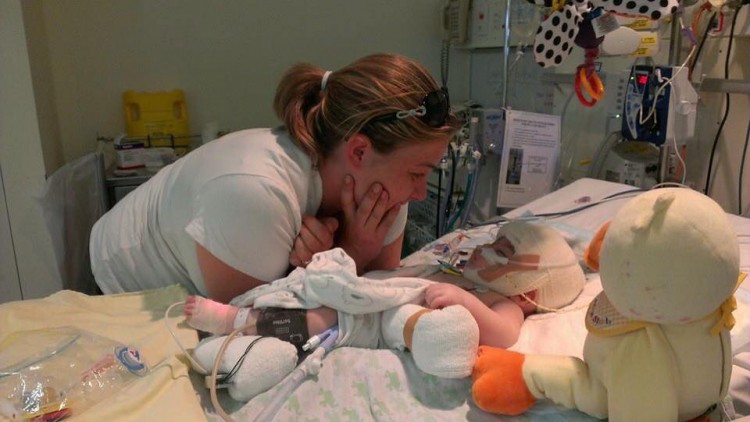 A mom stands over a little boy, who's laying in a hospital bed. 