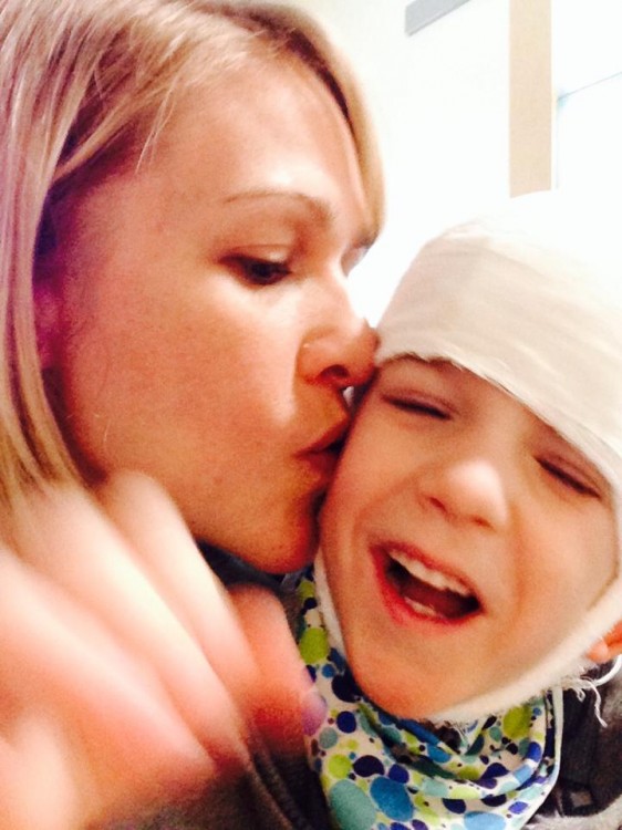 A woman kisses her son on the cheek. He has a bandage on his head. 