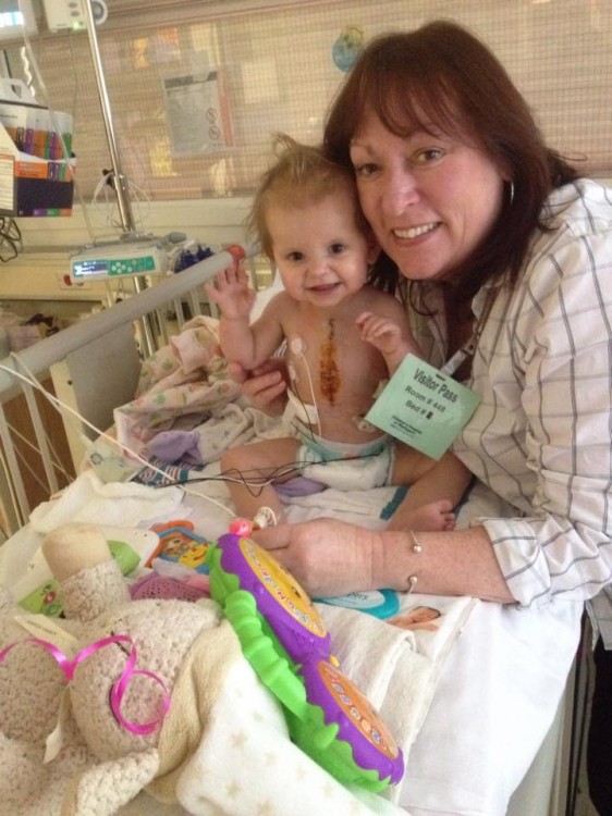 A mom smiles with her daughter, who sits in a crib in the hospital. 