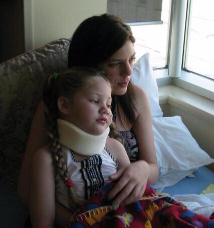 A little girl sits on her mom's lap. The girl wears a neck brace.