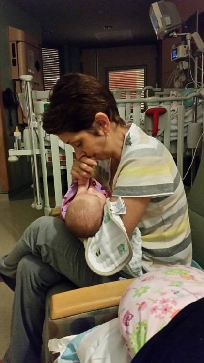 A mom sits on a chair on a hospital room, holding her baby.