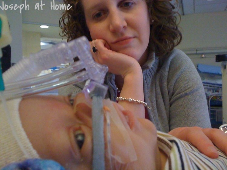 A woman looks at her child, who's hooked up to a breathing tube. 