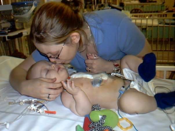 A mother kisses a little boy who lays on a hospital bed. 
