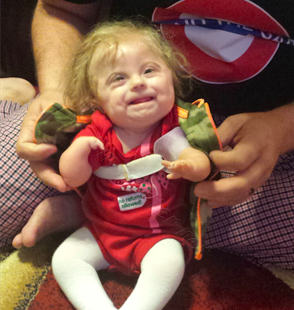 a baby girl sitting in her father's lap wearing a red onesie