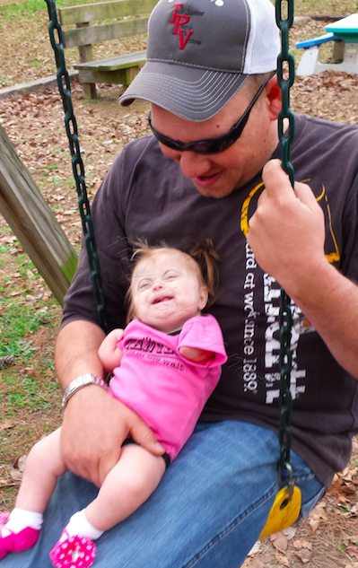 a small baby girl on her father's lap on a park swing