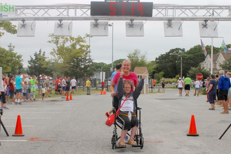 Eileen Benthal, pushing her daughter Johanna in a wheelchair crosses the finish line in the Jamesport Fire Department Sound-to-Bay footrace on August 23. (Photo credit: Denise Civiletti/RiverheadLOCAL.com)