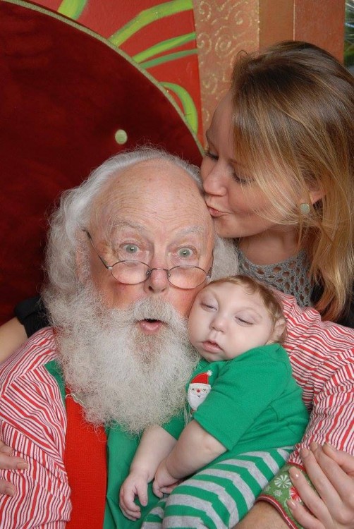 mother kissing santa's forehead while he holds her son