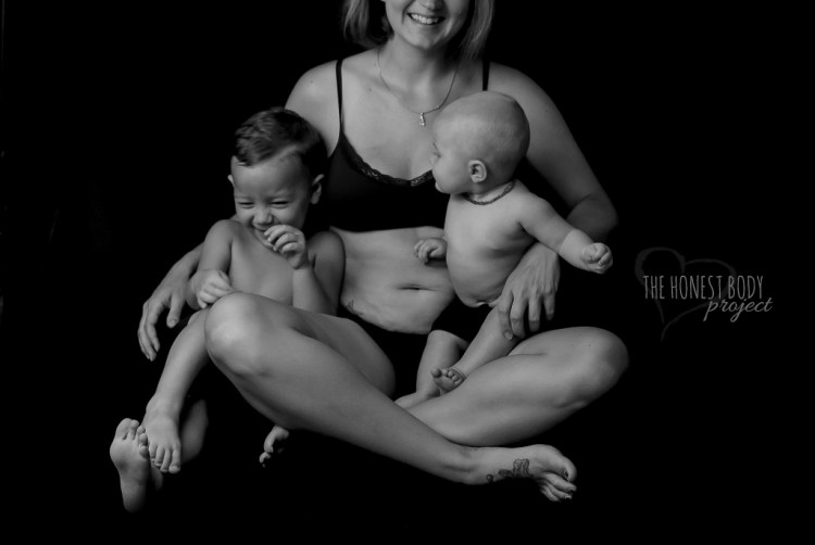 A mom sits on the floor holding her two kids