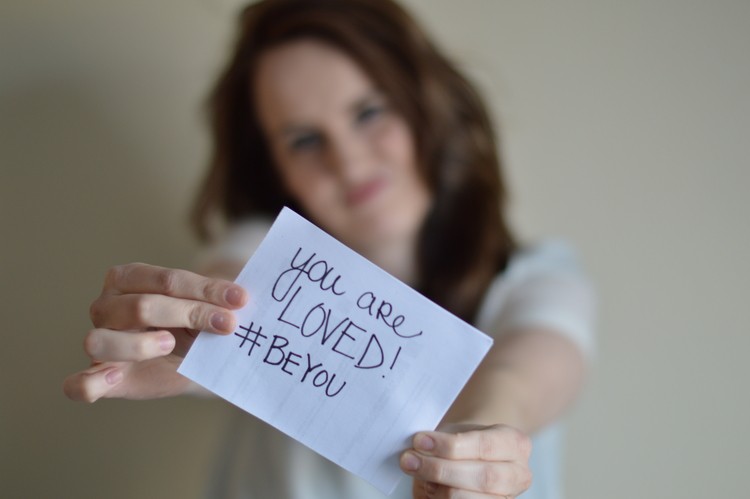 Julie holds up a sign that says, "You are loved. #BeYou."
