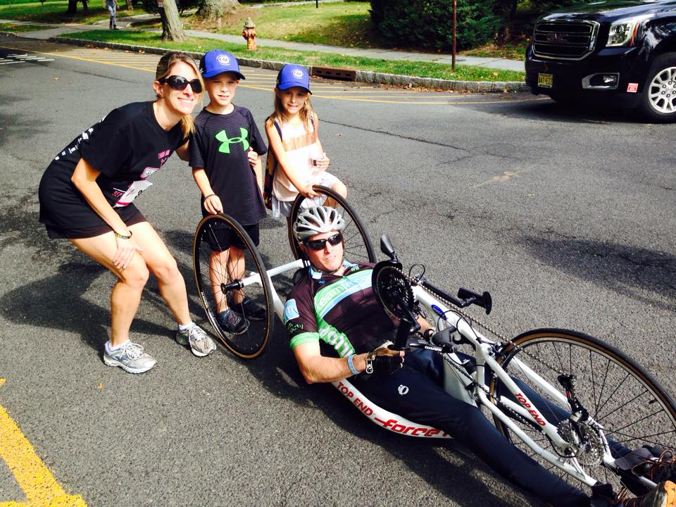 Man using a handcycle on the street next to his wife and two kids