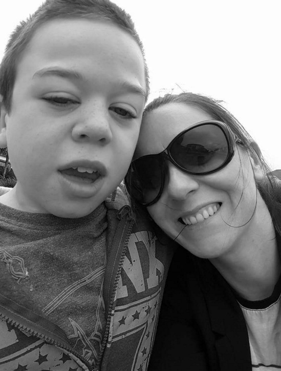 black and white photo of mom in sunglasses and her son. She has her head on her son's shoulder.