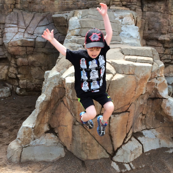boy wearing baseball cap jumping near a rock