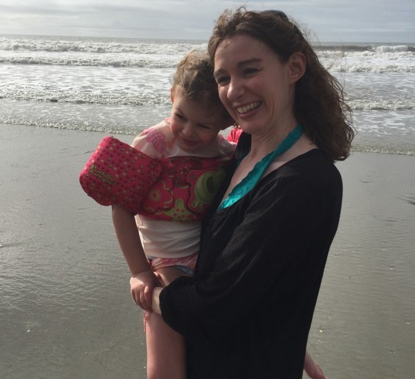 Mom holding her daughter. They're on a beach.