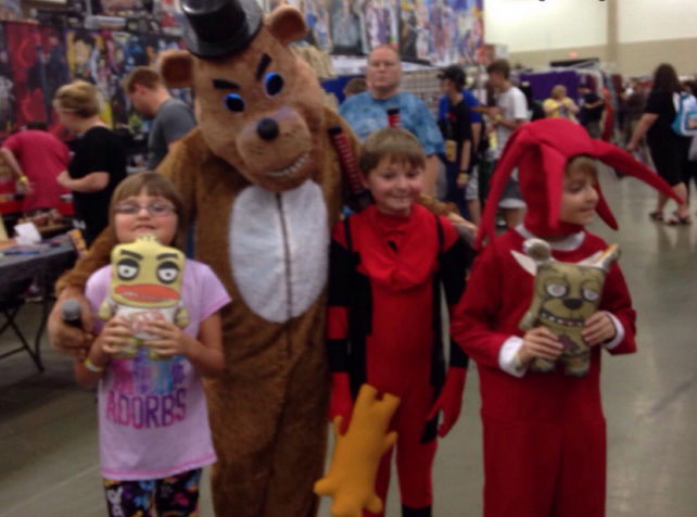 Kids posing with person in a bear costume at a comic convention