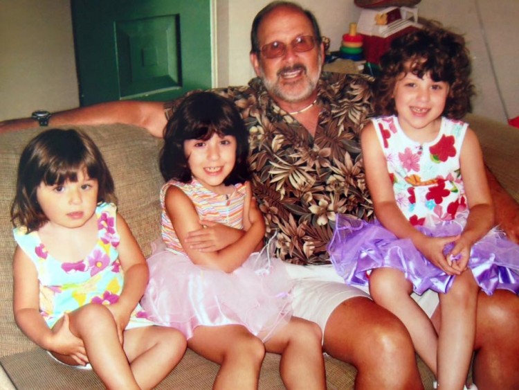 grandfather sitting on couch with three young girl grandchildren