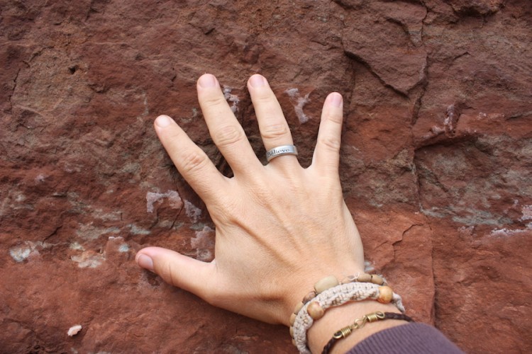 Fiona's hand placed on a rock. Her silver ring says "believe."