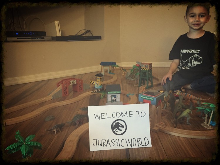 boy with train set and jurassic world sign