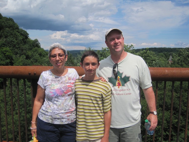 husband, wife and son in front of mountains