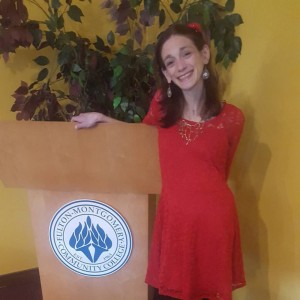 Amy at the Fulton College Podium, smiling and wearing a red dress