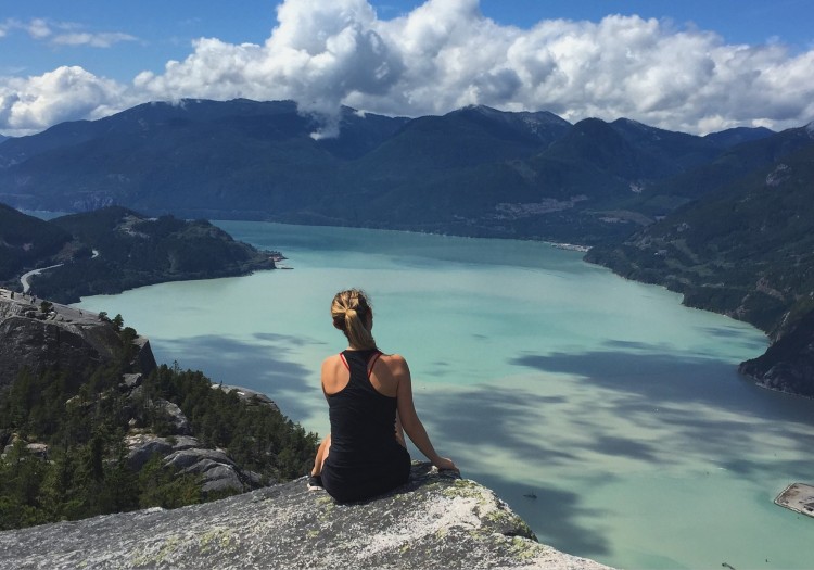 woman sitting on rock looking at mountains and lake