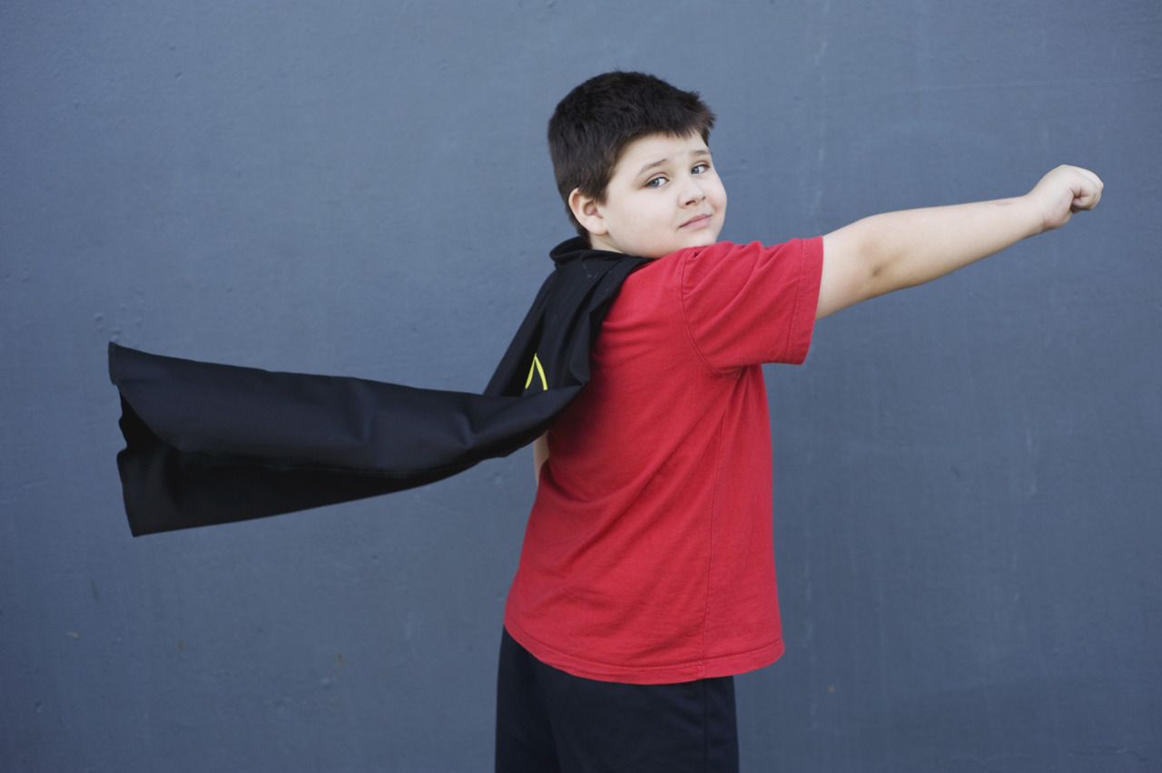 boy in cape poses like superman