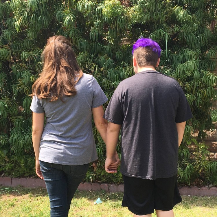 Shawna and her son, standing outside, view from the back. Her son has purple hair.