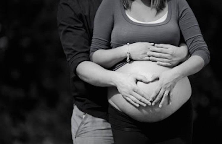 pregnancy photo of husband and wife with their hands making a heart on her belly