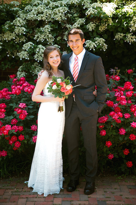 Libby and her husband on their wedding day, standing in front of two rose bushes.