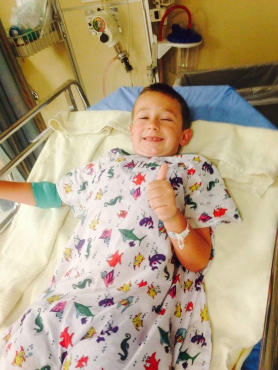 author's son lays in hospital bed giving a "thumbs up"