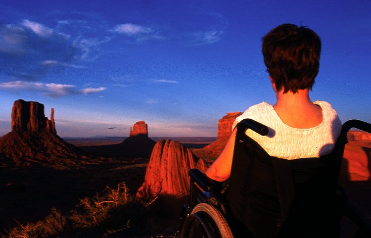 woman in wheelchair looking at sunset over desert