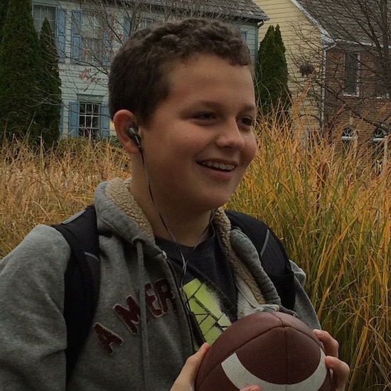 teen boy with headphones and backpack holding a football