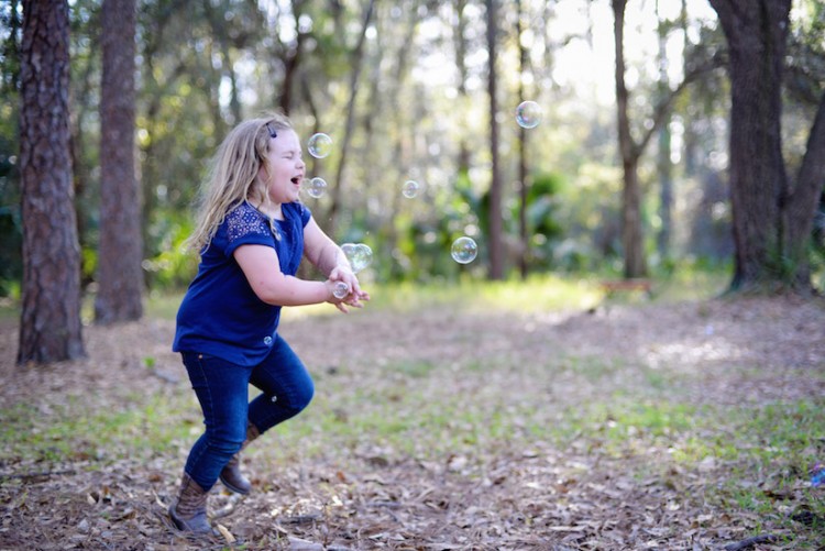 young girl chasing bubbles in the woods