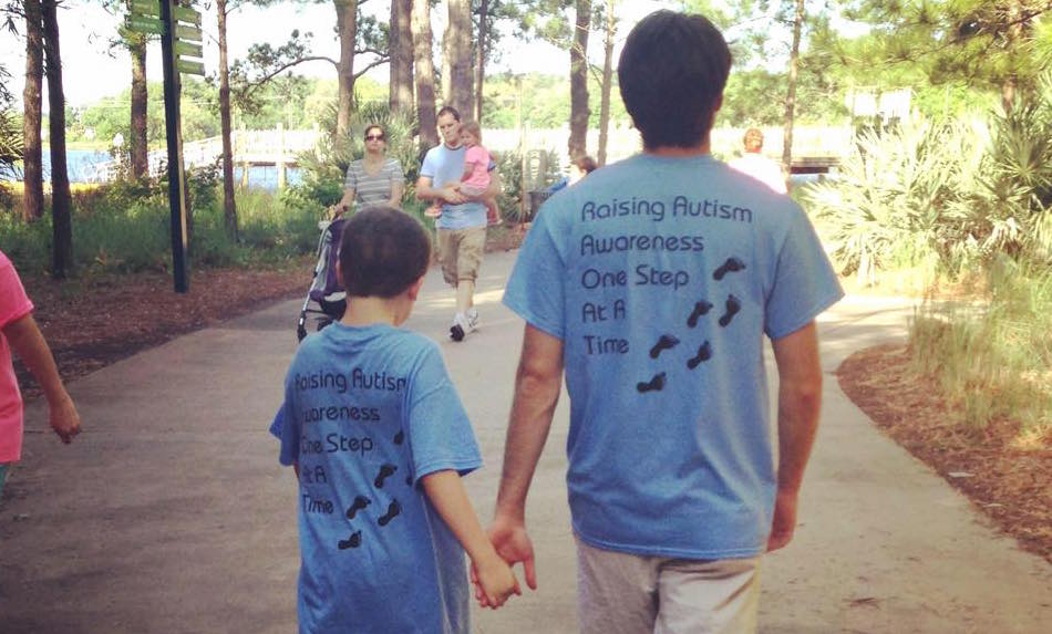 Two brothers walking hand in hand at the zoo both wearing t-shirts that read Raising Autism Awareness One Step At A Time