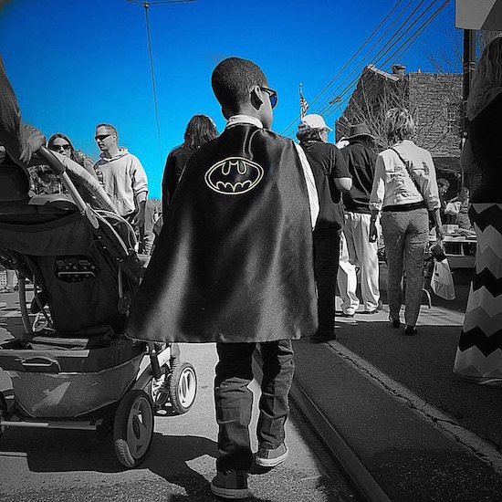 boy walking through crowd wearing superhero cape