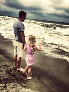 father and daughter holding hands standing on the beach looking at the waves