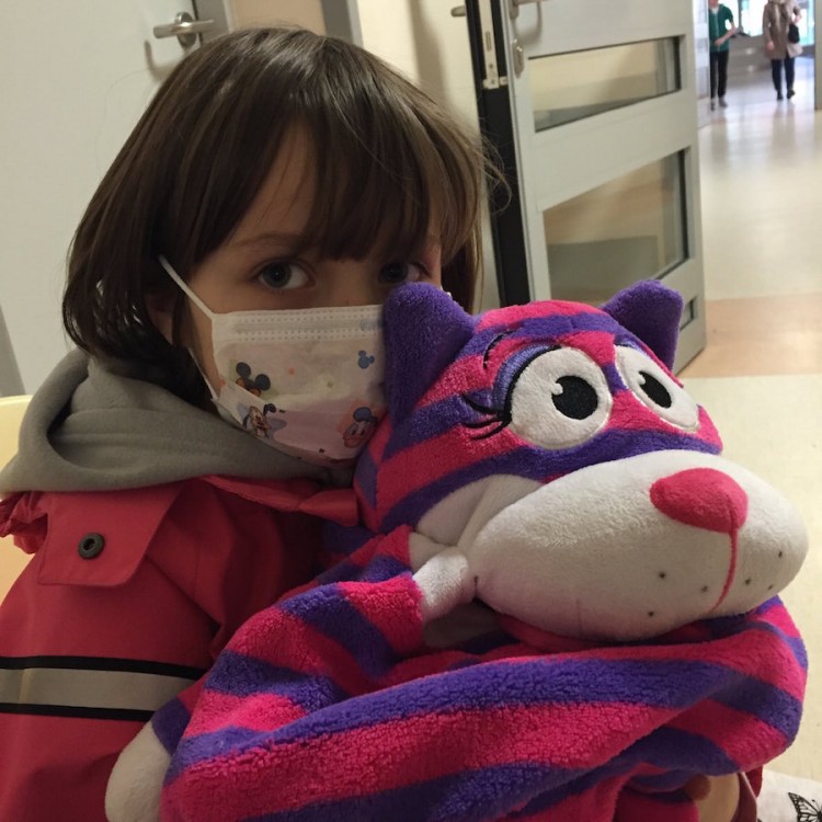 girl wearing hospital mask holding pink and purple stuffed animal