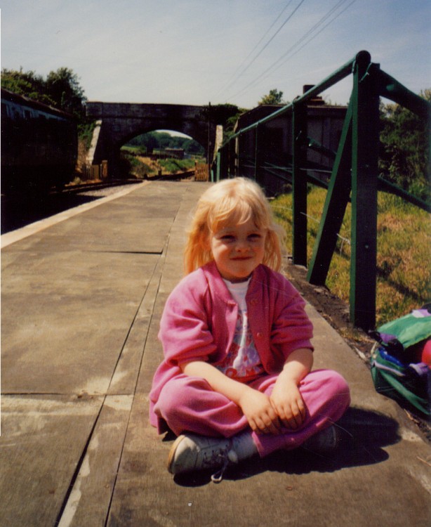 a young girl in a pink outfit sitting on a bridge