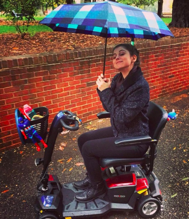 Liv in her scooter, holding an umbrella.