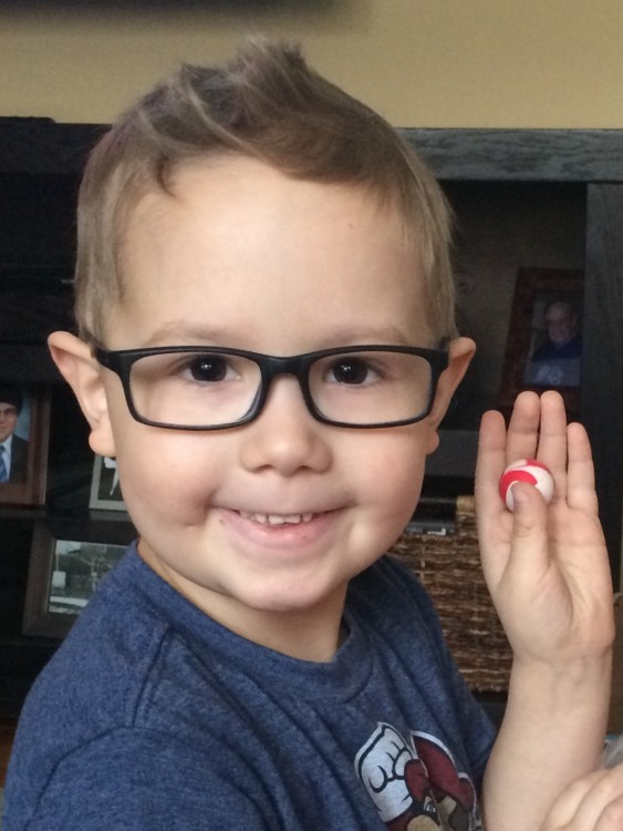 little boy in glasses holding up a small toy