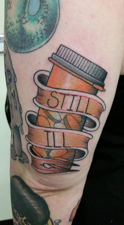 tattoo on arm of pill bottle that says Still Ill