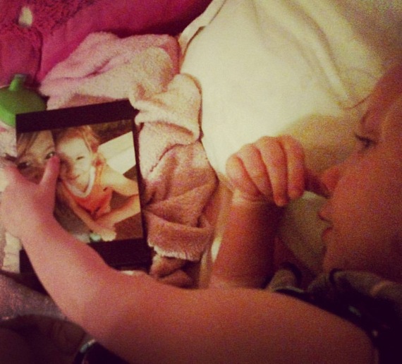 young girl lying in bed looking at frame photo of her with her mother