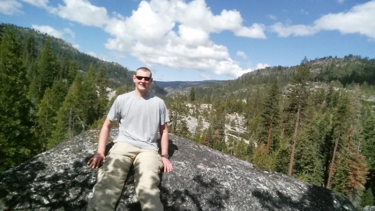 man sitting on rock with mountain view behind him
