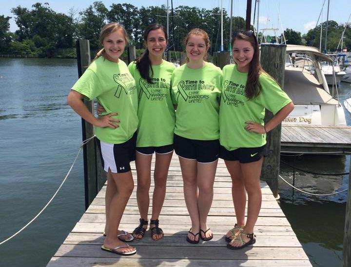 four teen girls wearing green shirts standing on a dock