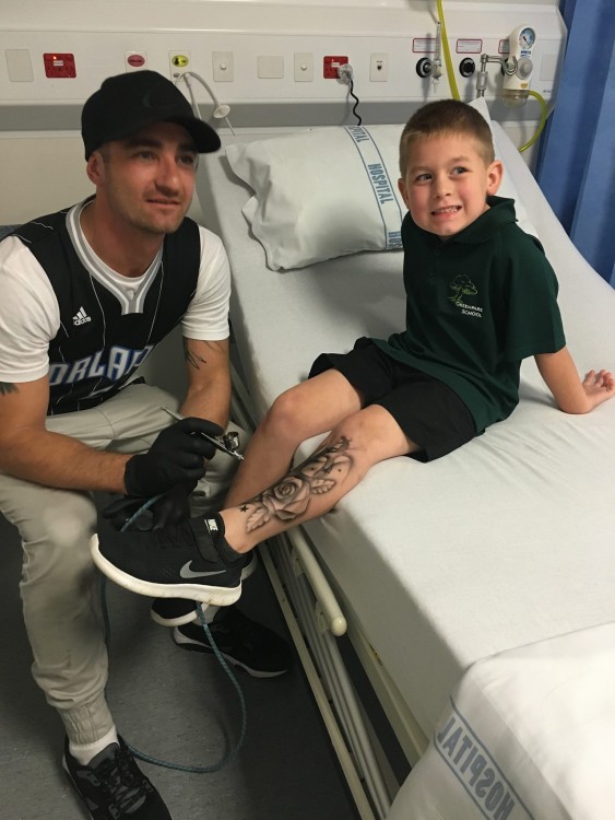 Lloyd tattooing a young boy sitting on a hospital bed