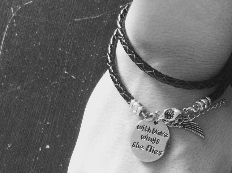 Close up of a bracelet that reads: With brave wings she flies