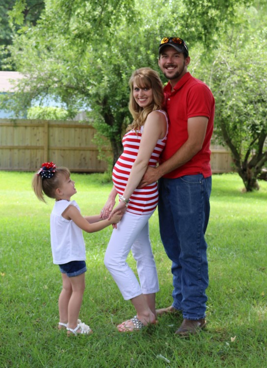 man standing behind pregnant woman who's holding hands with young girl