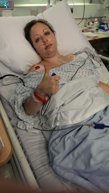 woman lying on hospital bed giving thumbs up